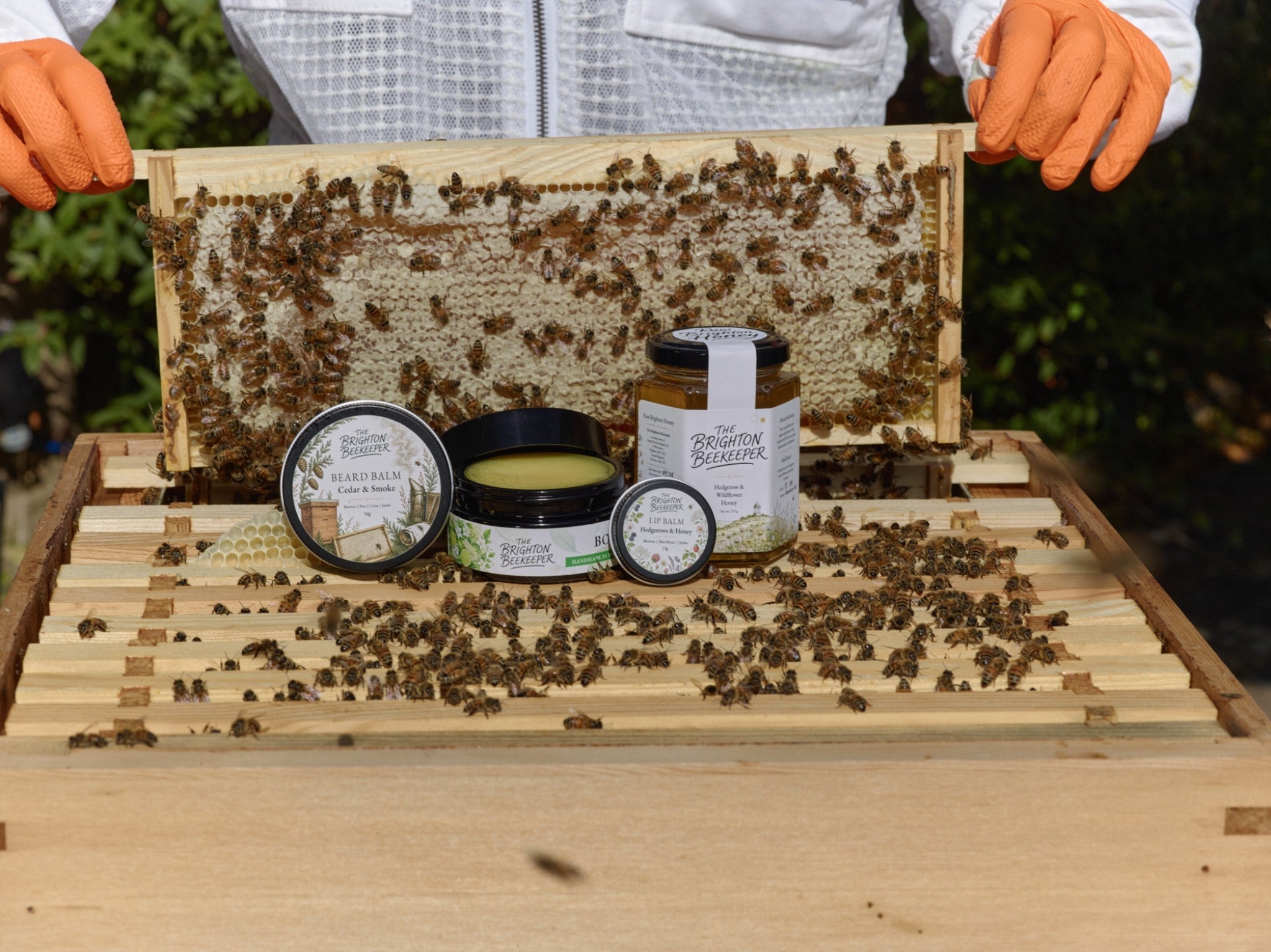 The Brighton Beekeeper balms, body butter and honey beside a frame of capped honey