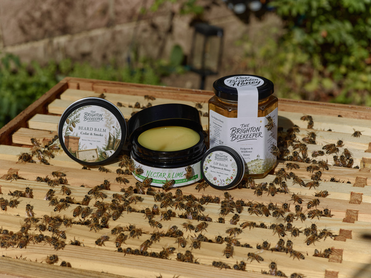 The Brighton Beekeeper body butter, beard balm and lip balm beside a jar of honey on an open cedar beehive
