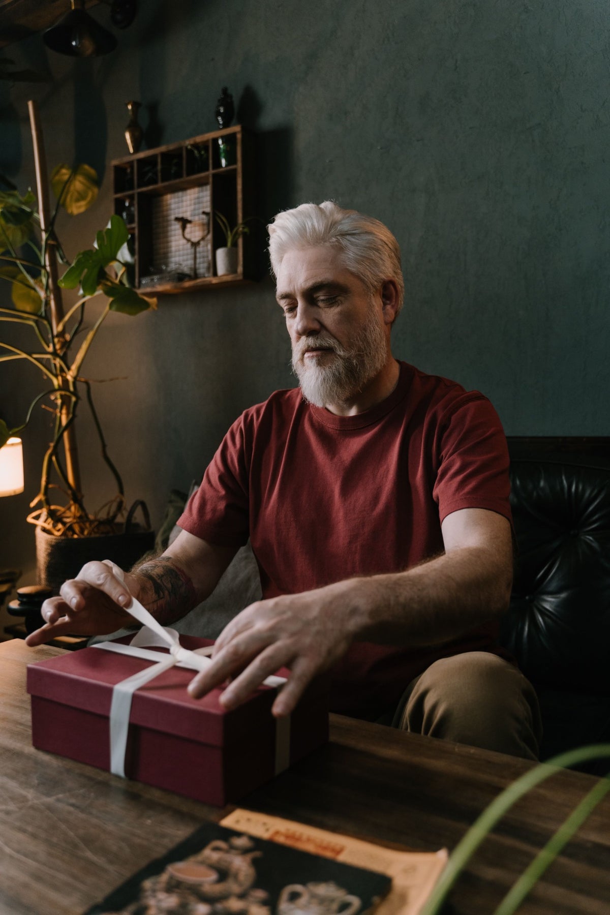 A silver-haired man with a beard untying the ribbon on a gift box