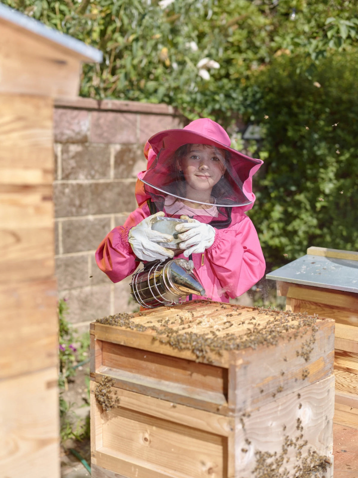 Sofia holding a beekeeper’s smoker beside a hive
