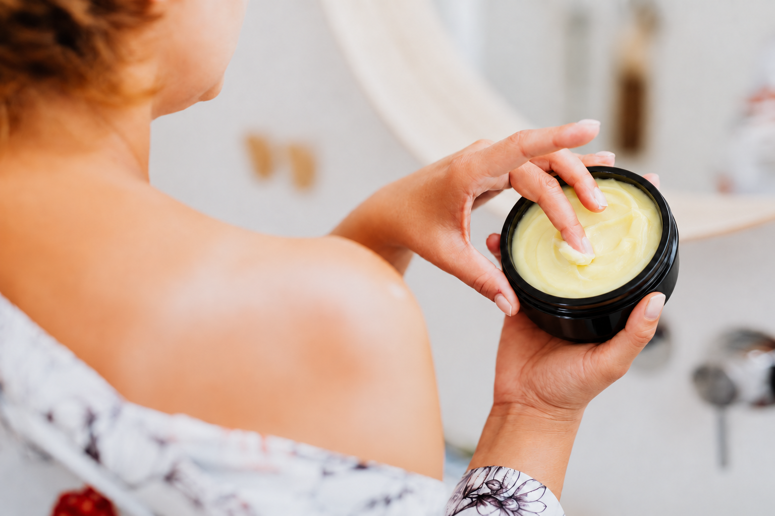 A person scooping body butter from an open black jar